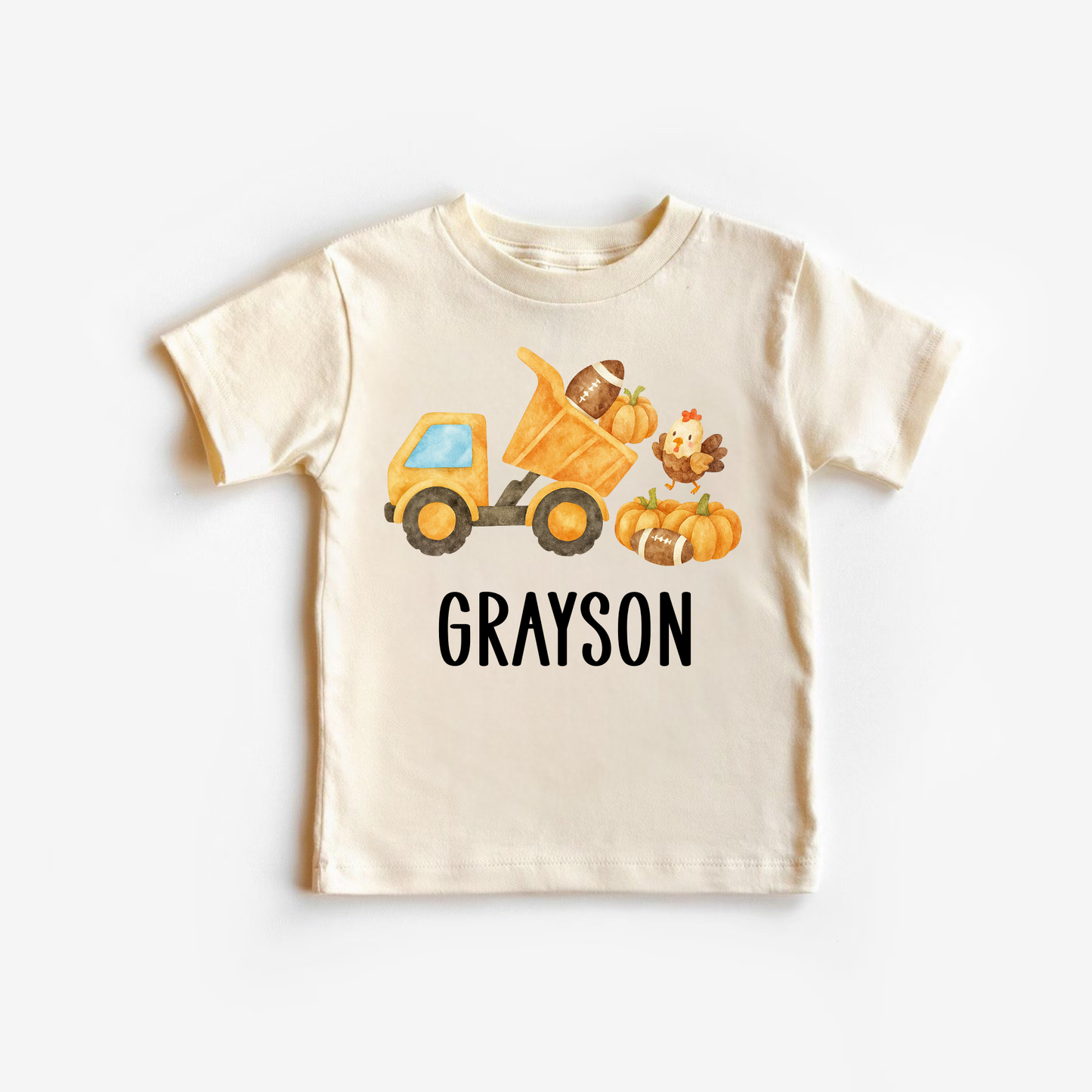 Beige t-shirt with a cartoon dump truck, pumpkins, and a turkey on a white background