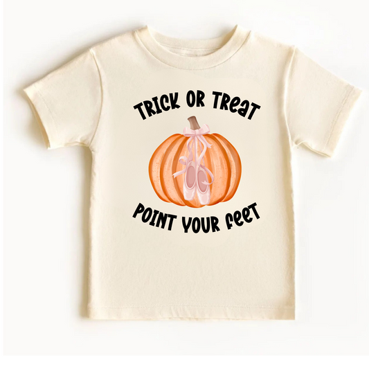 Cream-colored girls Halloween ballet T-shirt flat lay featuring a Trick or Treat Point Your Feet graphic with an orange pumpkin, pink ballet slippers, and a delicate pink bow. Cute ballerina Halloween shirt for girls, perfect for dance class parties, fall outfits, and little ballet lovers.