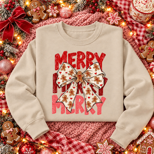 Sand gingerbread bow Christmas sweatshirt with distressed red and pink Merry Merry Merry lettering and gingerbread cookie ribbon, styled on a festive pink and red Christmas flat lay.
