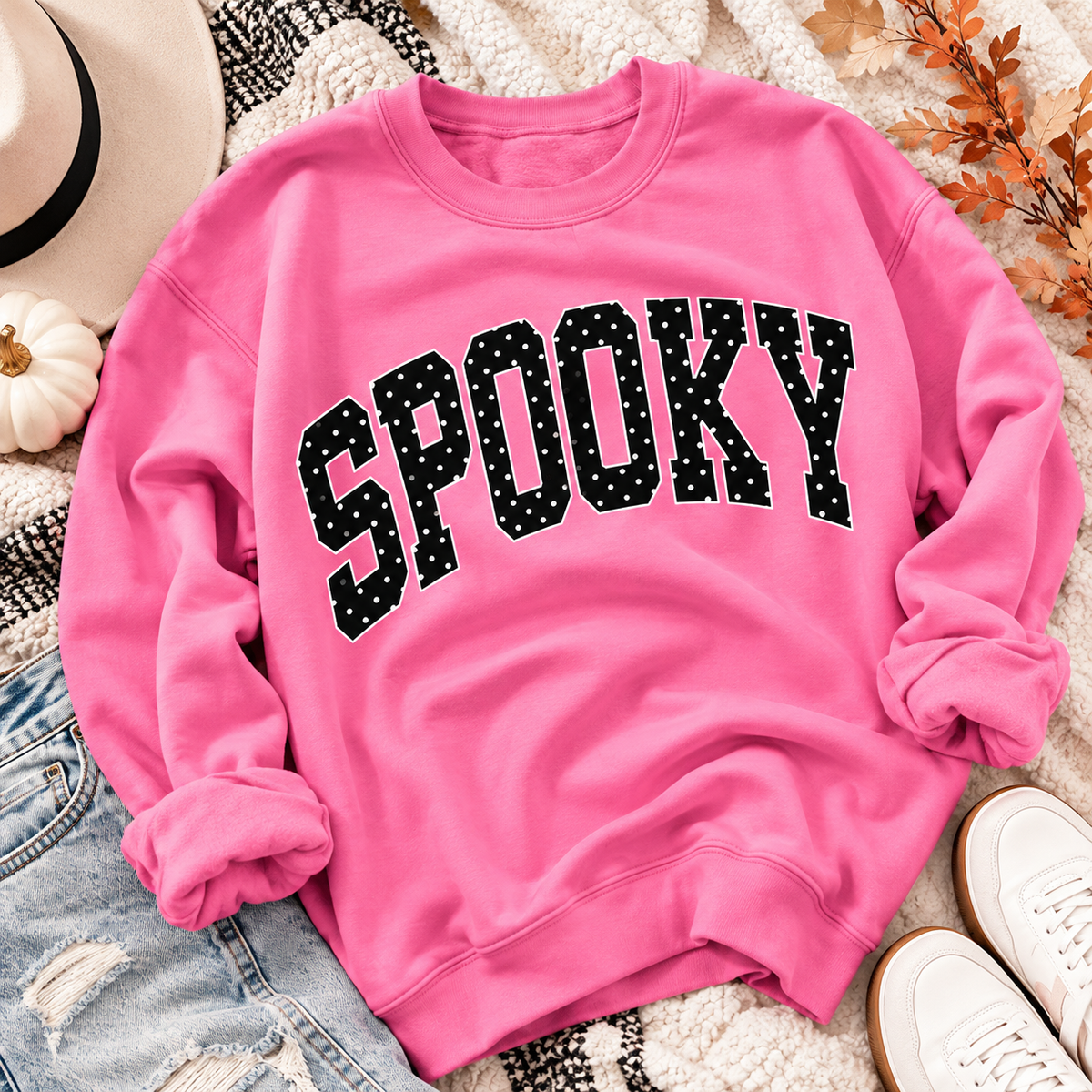 Bright pink Spooky Halloween crewneck sweatshirt with black polka dot varsity lettering styled in a cute spooky season fall flat lay.