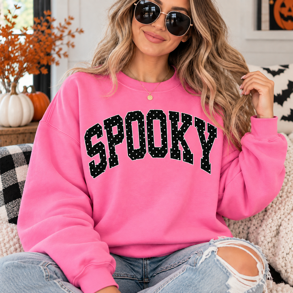 Woman wearing a bright pink Spooky Halloween sweatshirt with black and white polka dot varsity lettering styled with light wash jeans for a cute fall Halloween outfit.