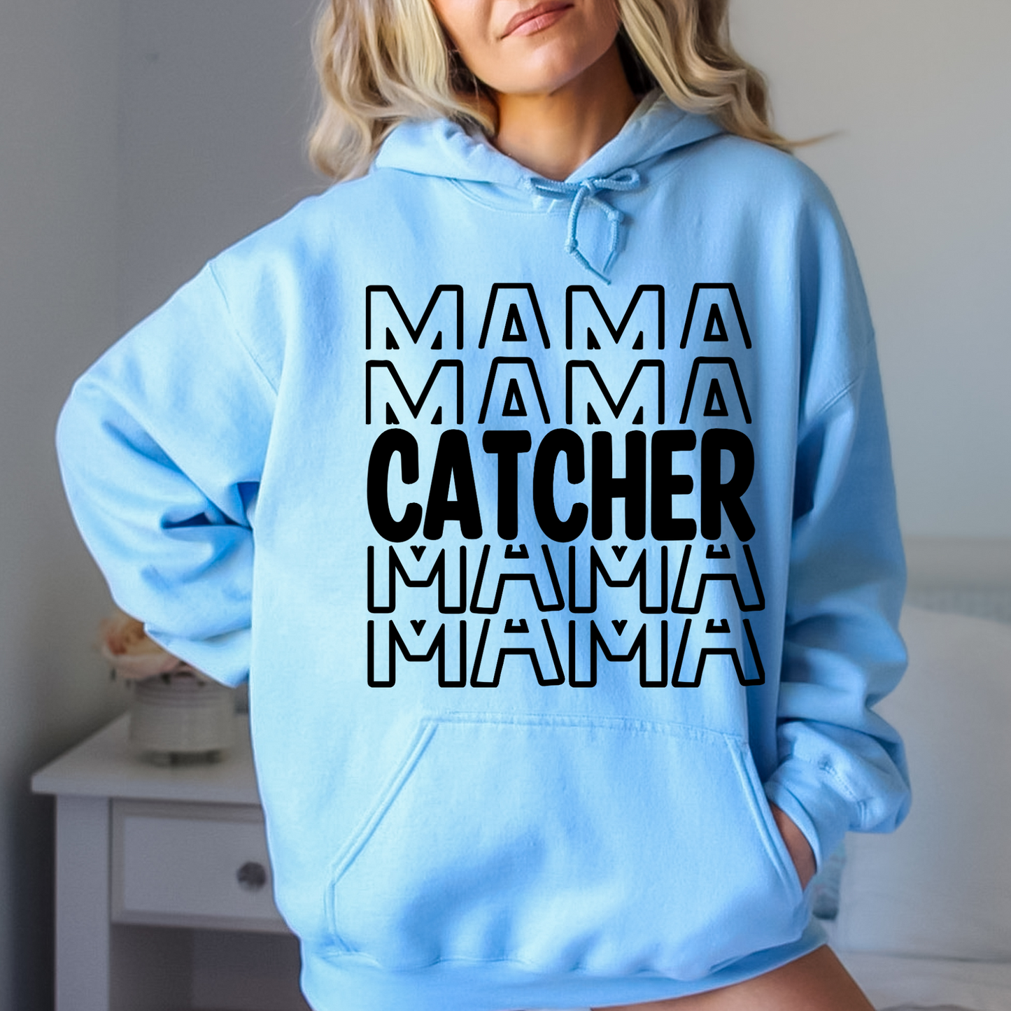 A comfortable and stylish baseball mom hoodie sweatshirt with the words 'Catcher Mama'. This baseball mom outfit is perfect for game day at the baseball game, featuring a cozy design that celebrates the role of a dedicated catcher mom.