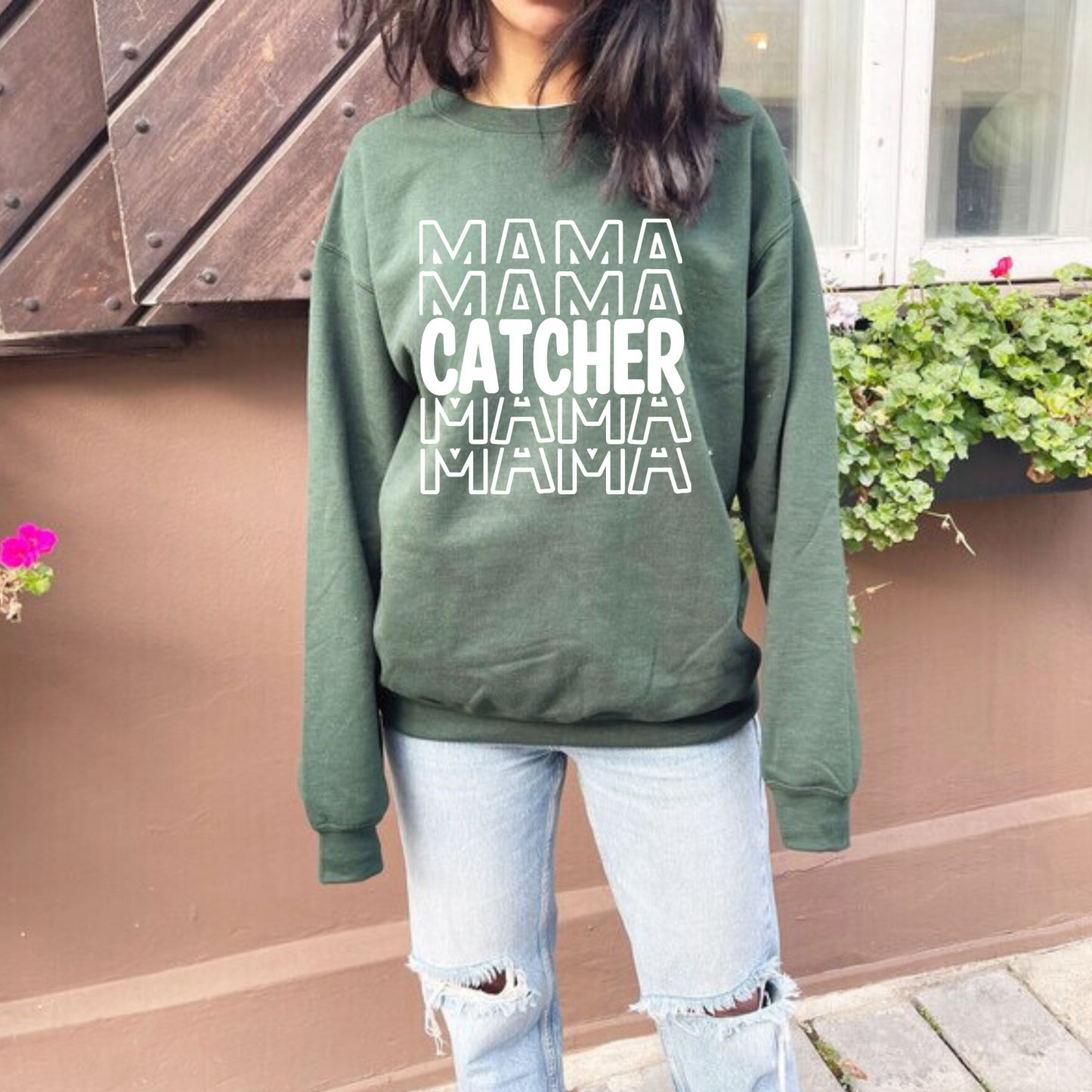 A comfortable and stylish baseball mom crewneck sweatshirt featuring the words 'Catcher Mama'. This baseball-themed sweatshirt is an ideal mom outfit for game days at the baseball game, celebrating the dedicated role of a catcher mom.