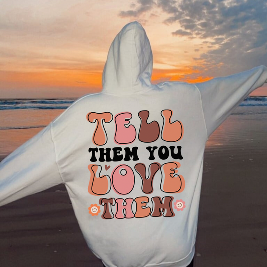 Woman wearing an oversized Pinterest aesthetic hoodie that says tell them you love them styled for a cozy neutral outfit